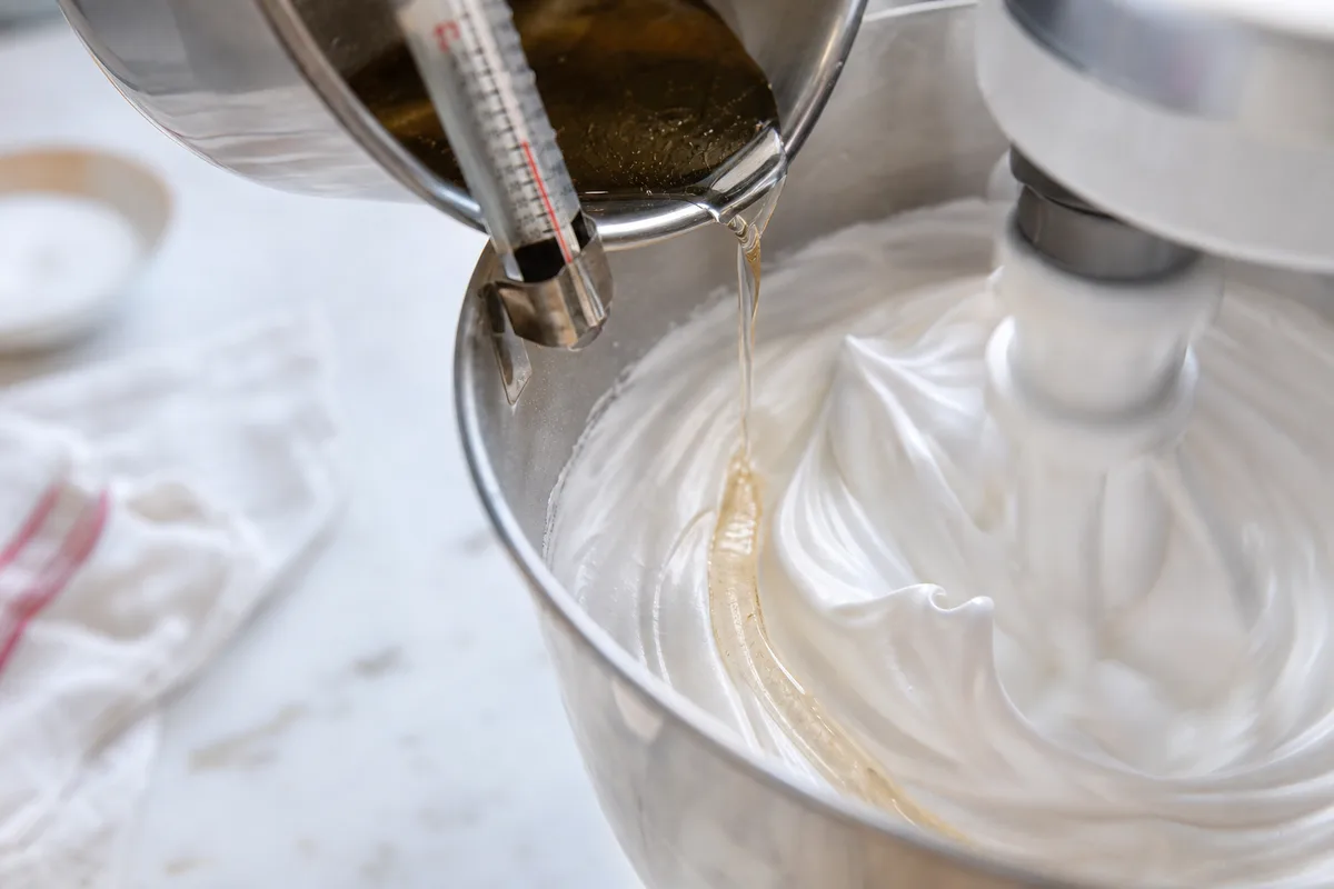 Filet de sirop de sucre chaud versé sur des blancs montés dans un bol de robot pâtissier, thermomètre à sucre visible